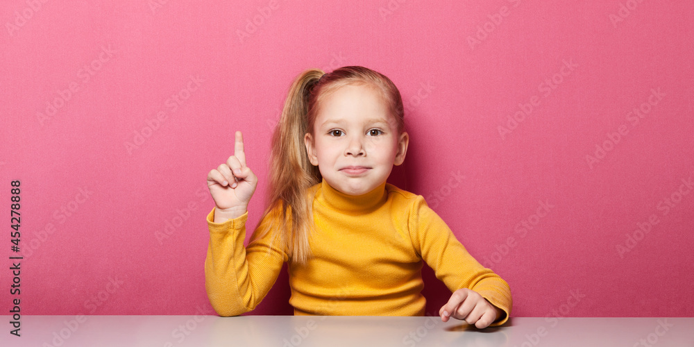 Girl is sitting at the table and shows her index fingers up