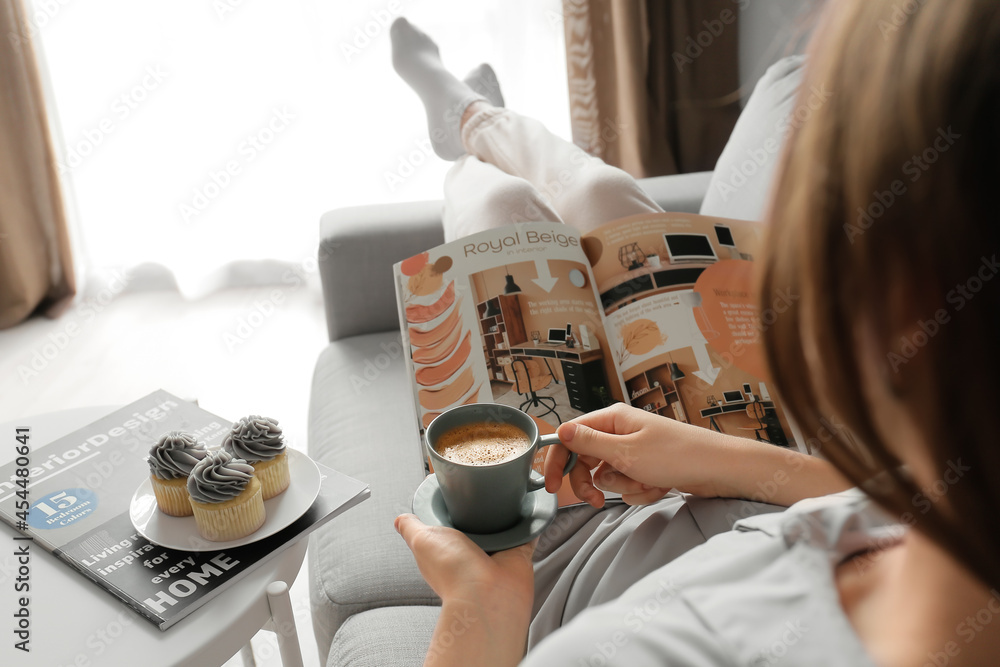 Young woman with cup of coffee reading magazine at home, closeup