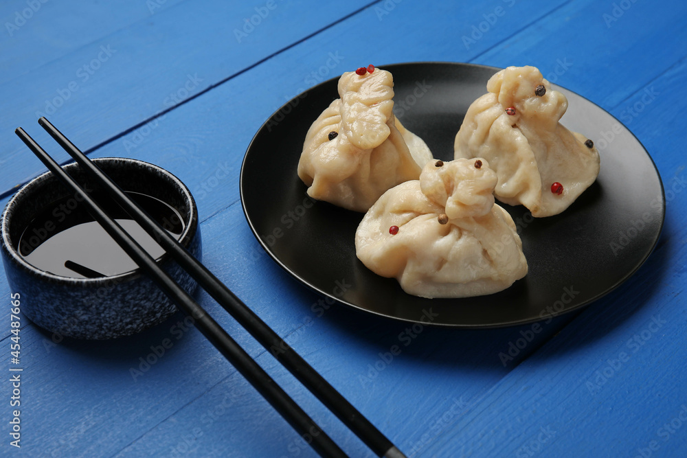 Plate with tasty dumplings, chopsticks and bowl of sauce on color wooden background, closeup