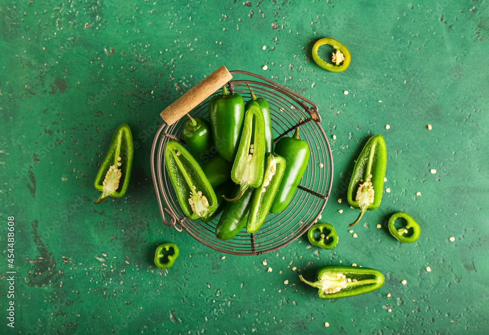 Basket with cut green jalapeno peppers on color background