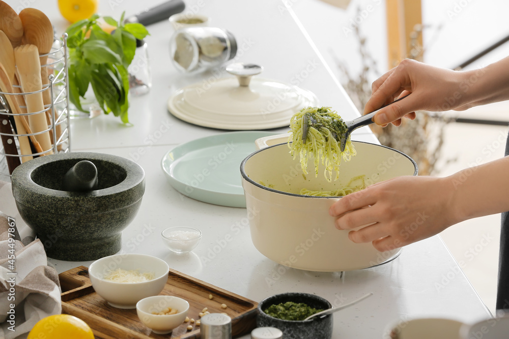 Woman cooking tasty pesto pasta at table