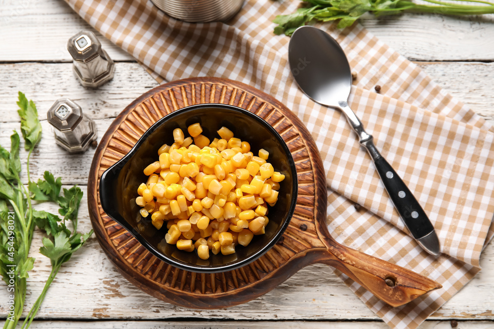 Bowl with corn kernels and spices on light wooden background