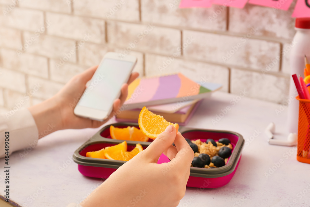 Pupil eating orange and using mobile phone at table