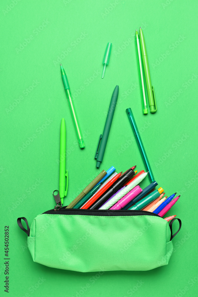 Pencil case with colorful markers and pens on color background