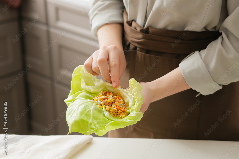 Woman preparing stuffed cabbage roll on table in kitchen, closeup