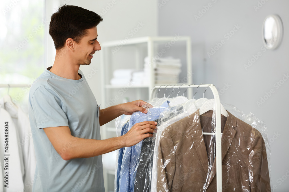 Male worker near rack with clothes at modern dry-cleaners