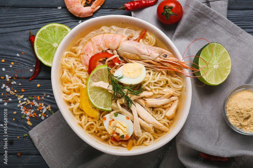 Bowl of tasty Thai soup with shrimps and chicken on dark wooden background