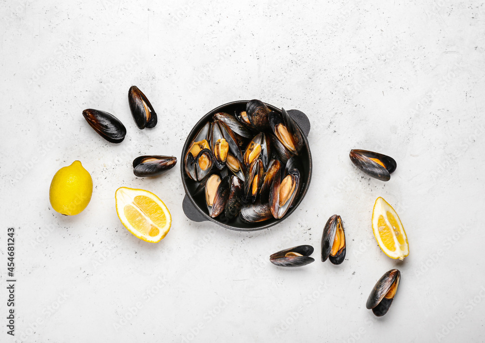 Frying pan with tasty mussels and lemon on light background