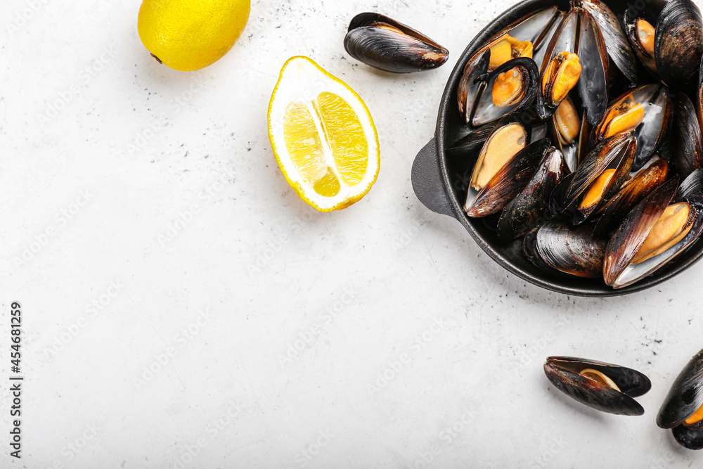 Frying pan with tasty mussels and lemon on light background, closeup