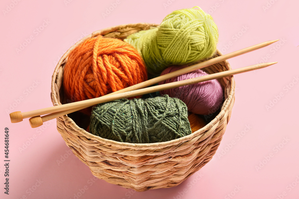 Basket with knitting yarn and needles on color background