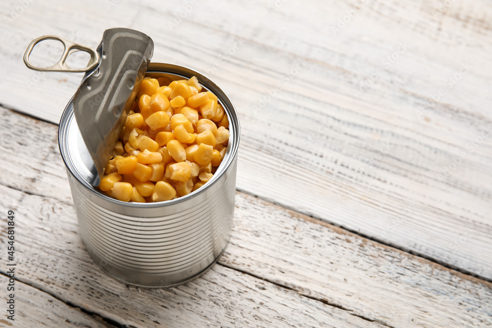 Tin can with corn kernels on light wooden background