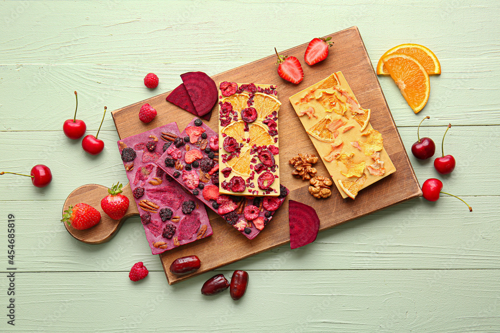 Handmade chocolate bars with fruits, berries and nuts on color wooden background