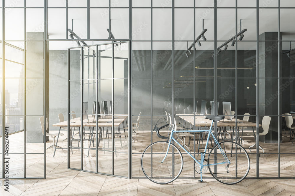 Modern glass partition and bike in stylish coworking office interior with city view and daylight. 3D