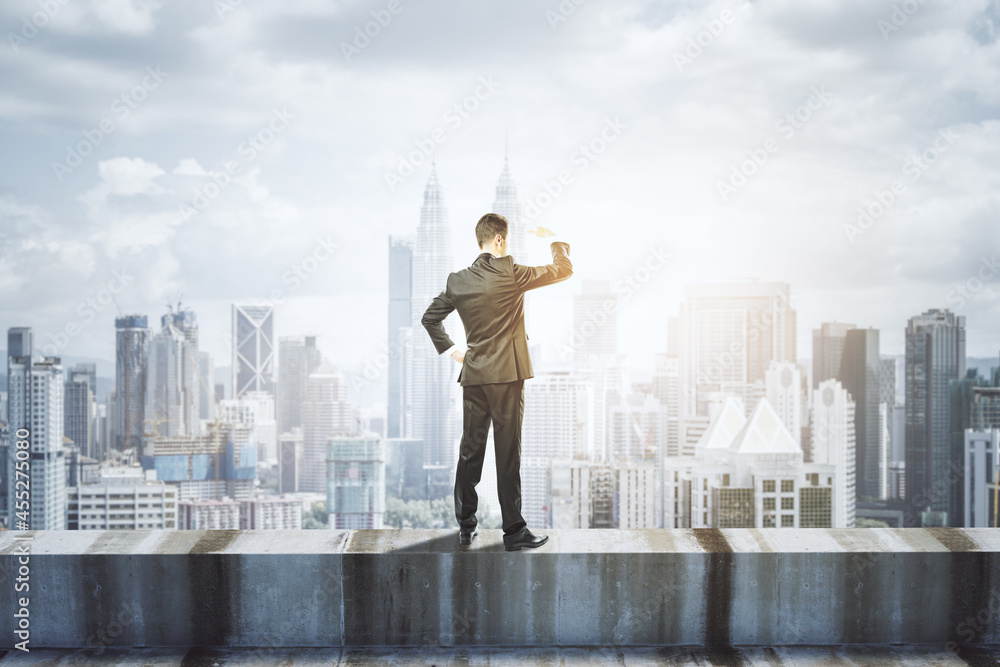 Back view of young business man standing on concrete edge of building on city background with mock u