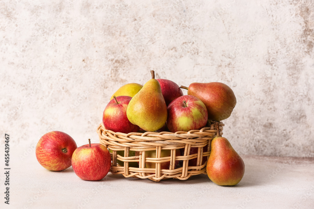 Basket with ripe pears and apples on light background