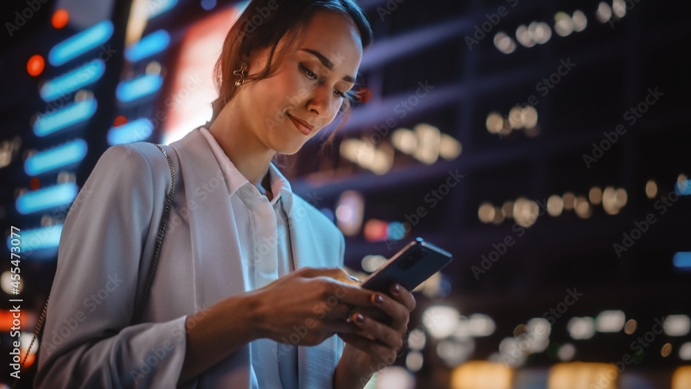 Beautiful Young Woman Using Smartphone Walking Through Night City Street Full of Neon Light. Portrai