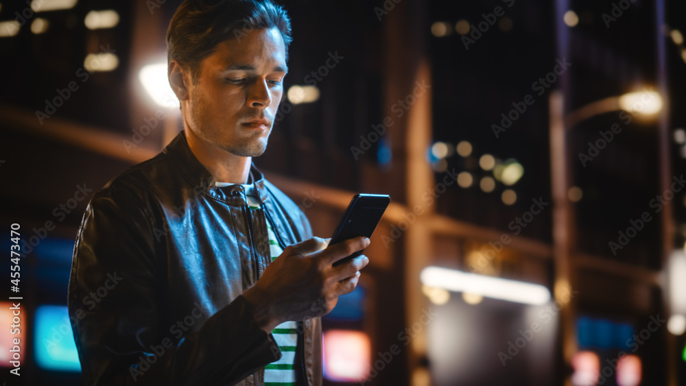 Portrait of Handsome Young Man Using Smartphone Standing in the Night City Street Full of Neon Light