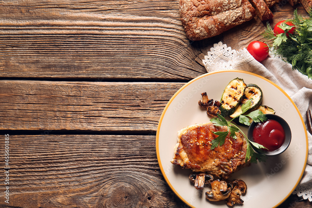 Plate with tasty pork steak, tomato sauce and grilled vegetables on wooden background