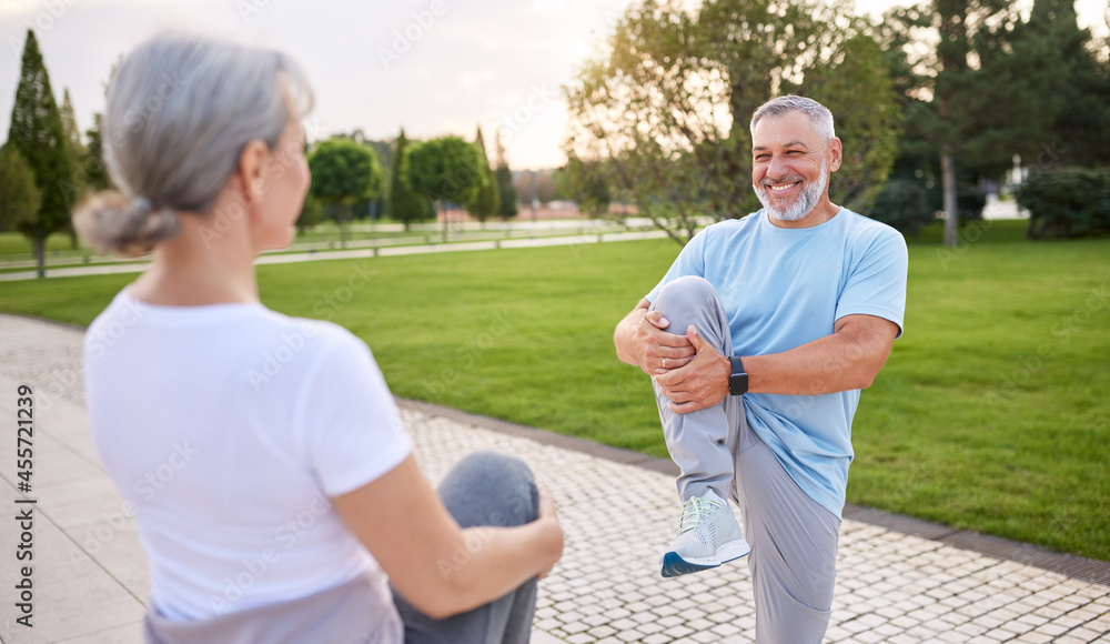 Healthy senior couple of husband and wife doing stretching exercises together in city park