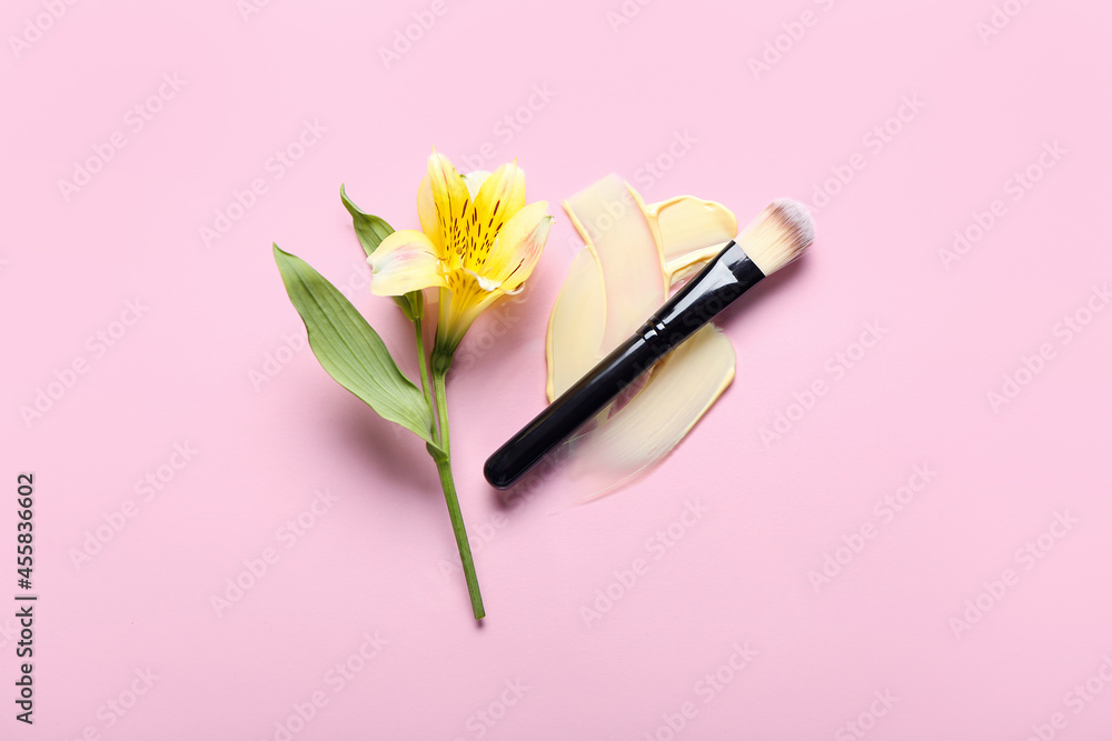 Brush with makeup foundation samples and flower on color background