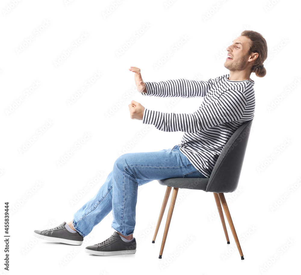 Young man with imaginary steering wheel sitting on chair against white background