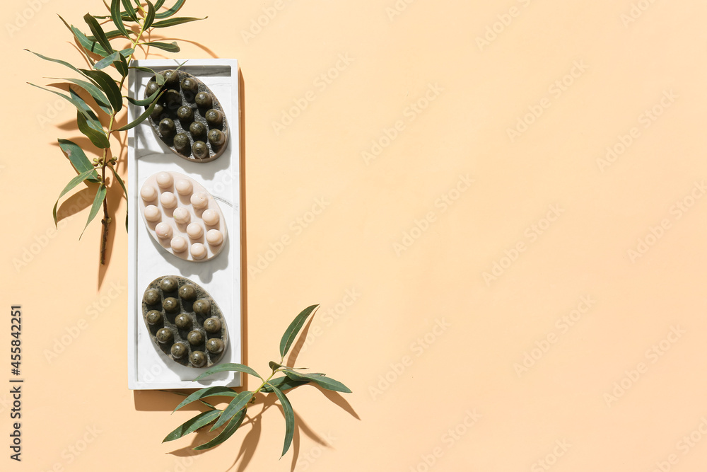 Board with massage soap bars and olive branches on color background