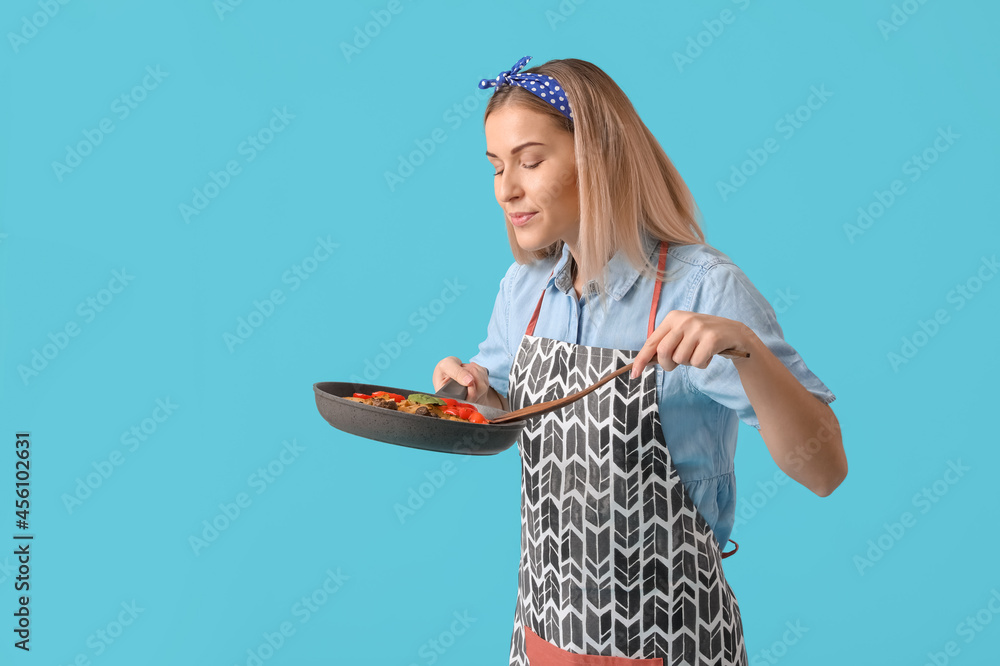 Young housewife with tasty dish in frying pan on color background