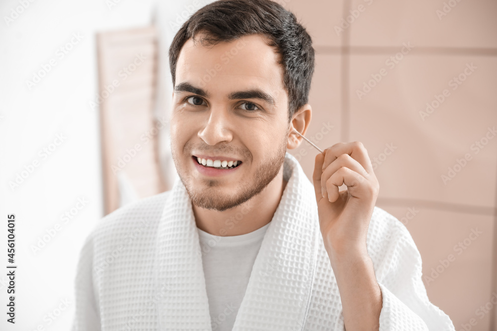 Young man cleaning ears with cotton bud in bathroom