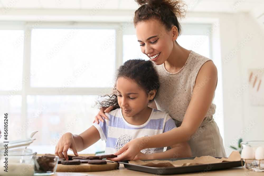 African-American little girl and her mother preparing cookies in kitchen