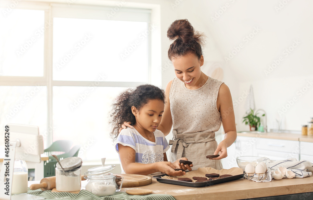 African-American little girl and her mother preparing cookies in kitchen