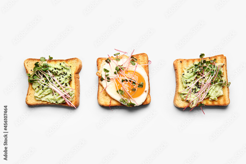 Tasty toasts with avocado, fried egg and micro green on white background