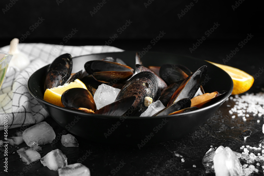 Bowl of tasty mussels with lemon and ice on dark background