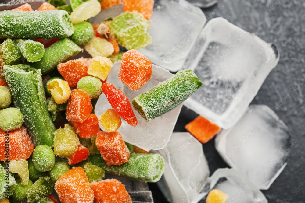 Mix of frozen vegetables and ice cubes on dark background, closeup