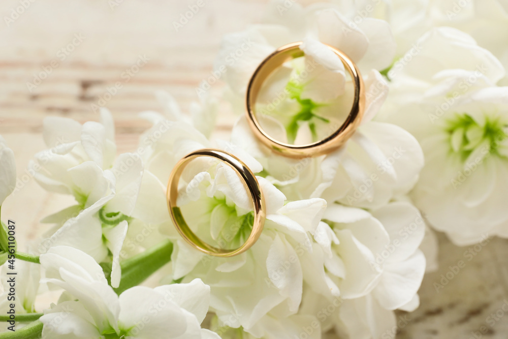 Wedding rings and beautiful flowers on light wooden table