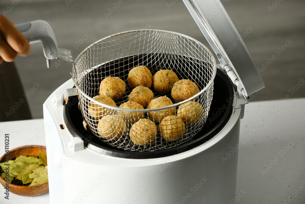 Woman holding basket with cod cutlets in deep fryer