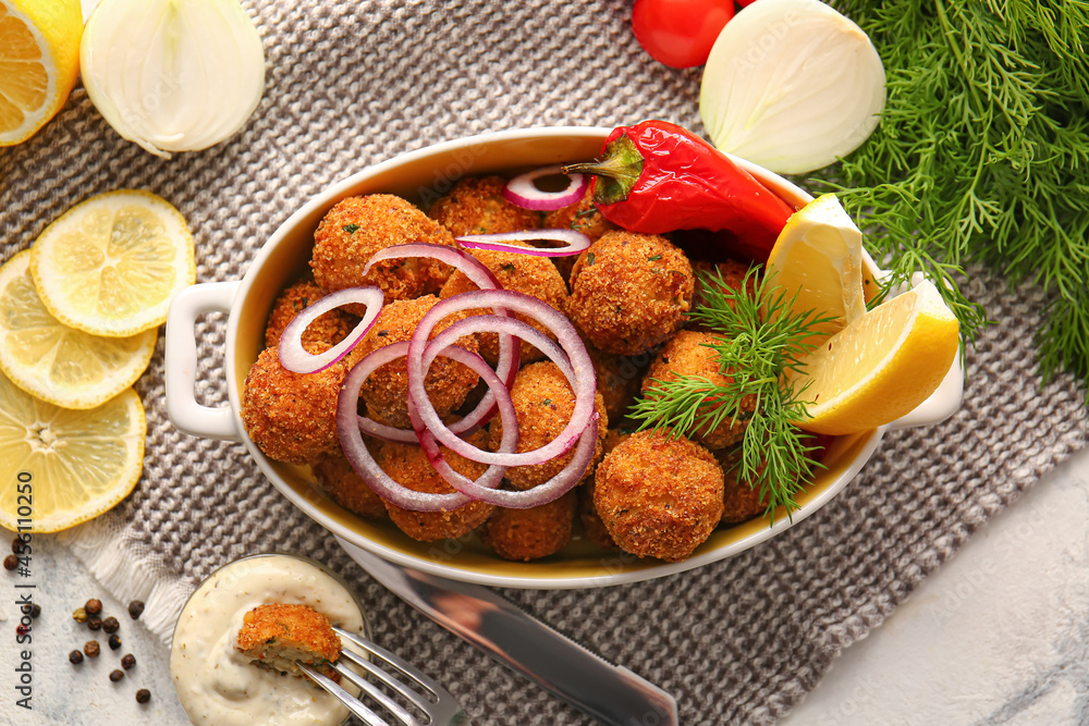 Baking dish with tasty cod cutlets and sauce on light background