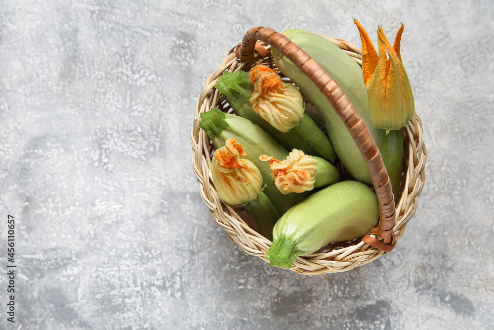 Wicker basket with fresh zucchini and flowers on grey background