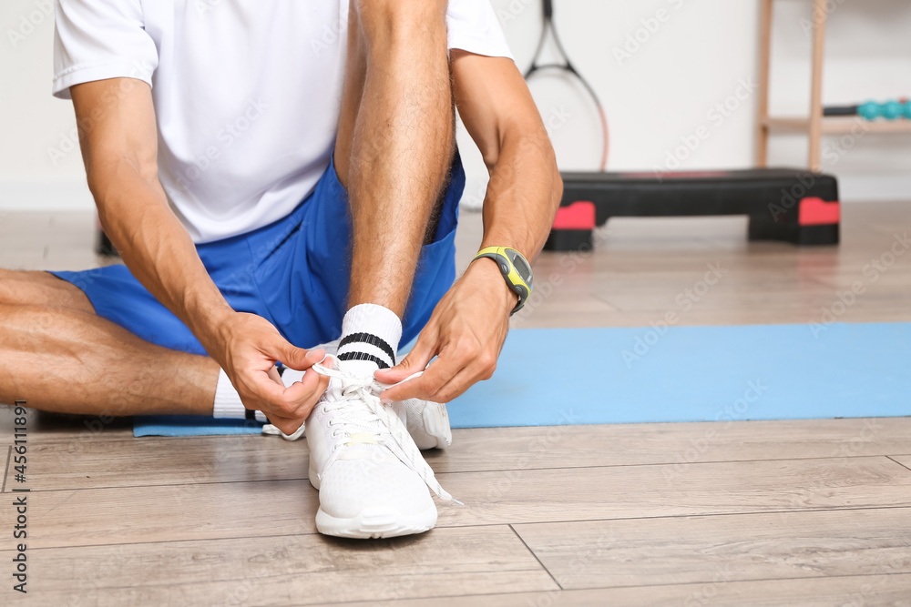 Sporty young man tying shoe laces in gym