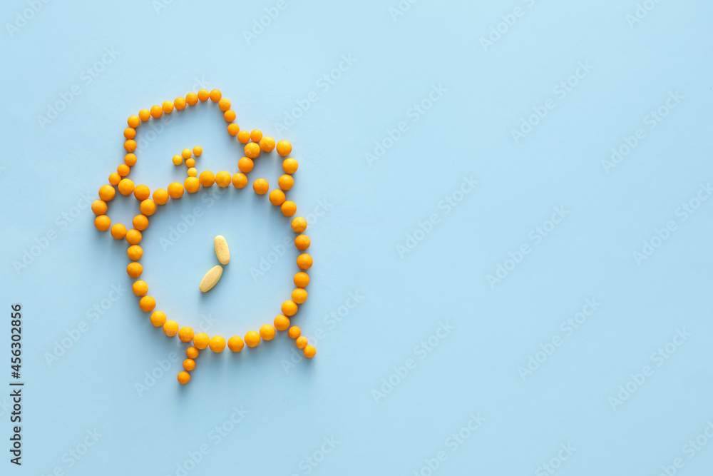 Alarm clock made of pills on color background