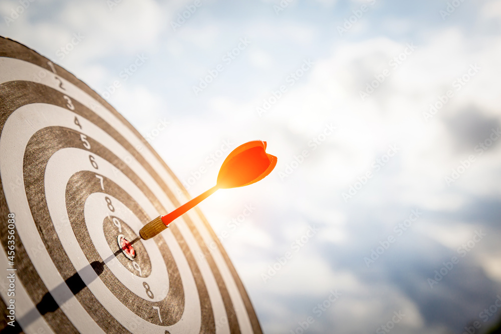 Close up shot red darts arrows in the target  of dartboard center on dark blue sky background. Busin