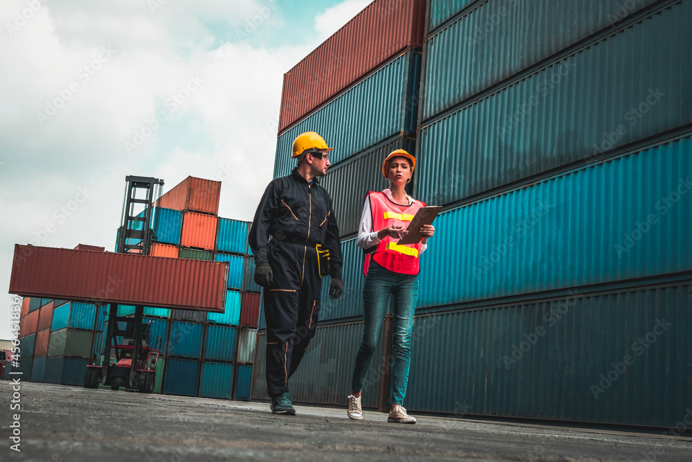 Industrial worker works with co-worker at overseas shipping container yard . Logistics supply chain 