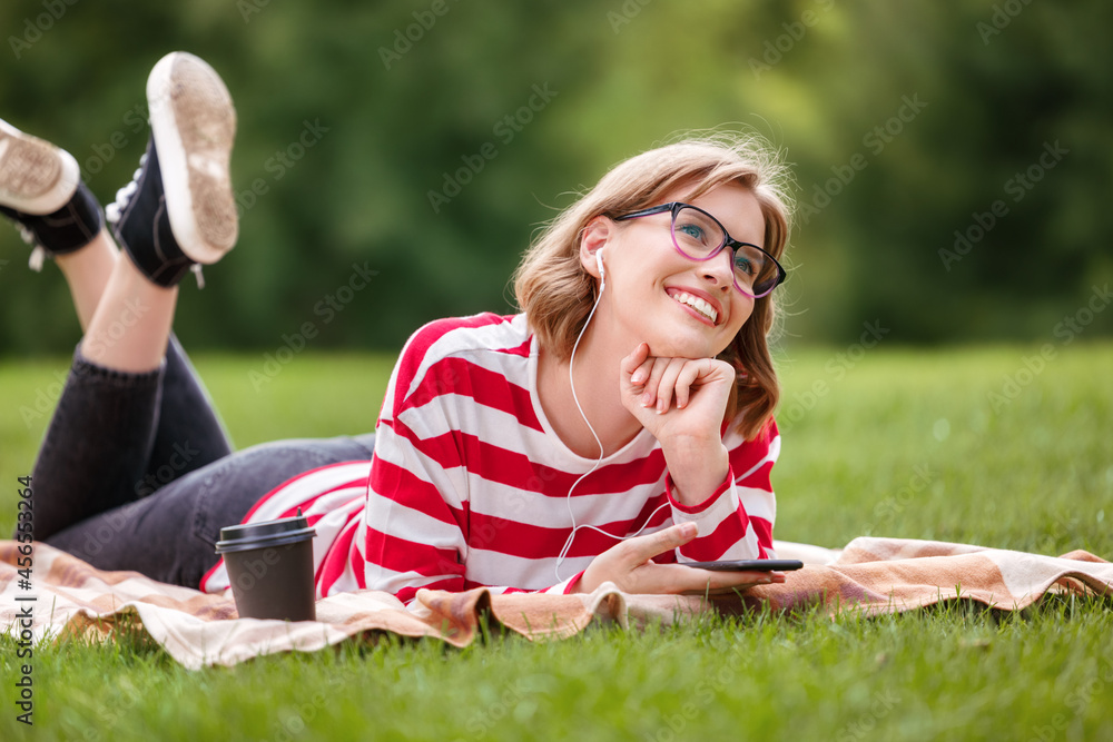 可爱的有远见的时髦女孩，穿着条纹衣服，戴着眼镜，躺在公园外面的毯子上