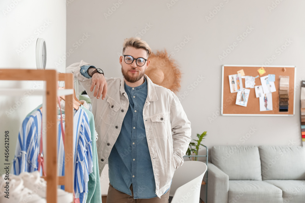 Male stylist near rack with clothes in studio