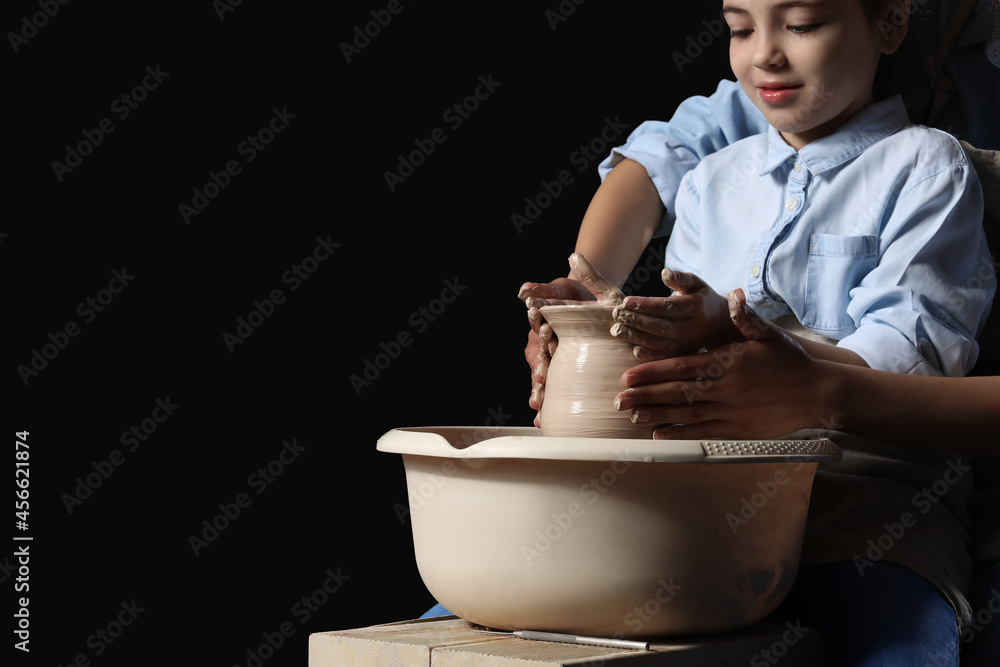 Little girl with her mother making ceramic pot on dark background