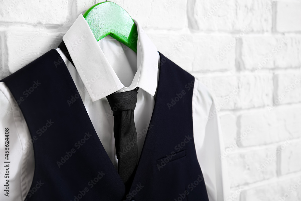 Hanger with stylish school uniform on white brick wall in room