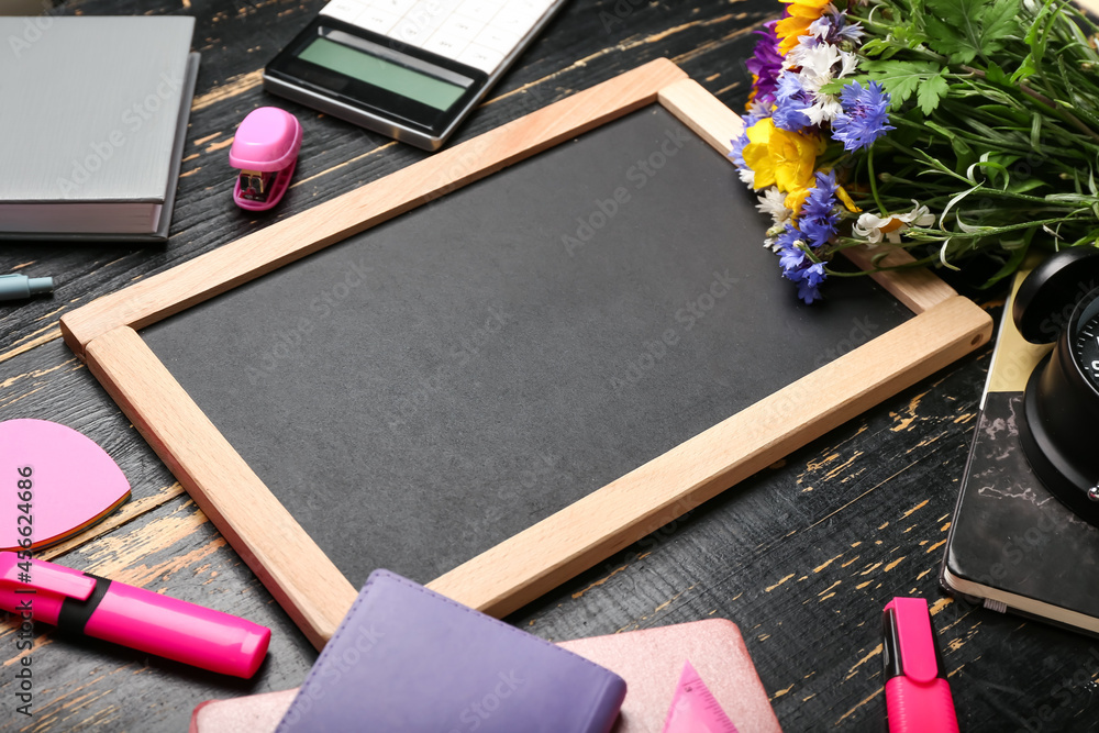 Blank chalkboard, flowers and stationery on dark wooden background, closeup. Teachers Day celebrati