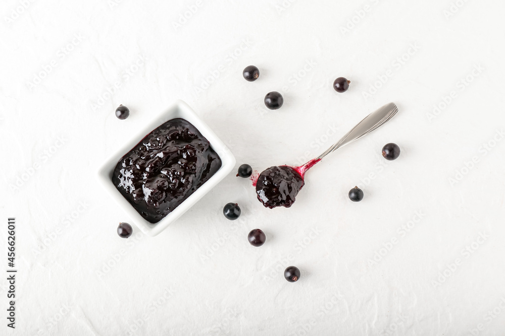 Bowl with black currant jam on light background