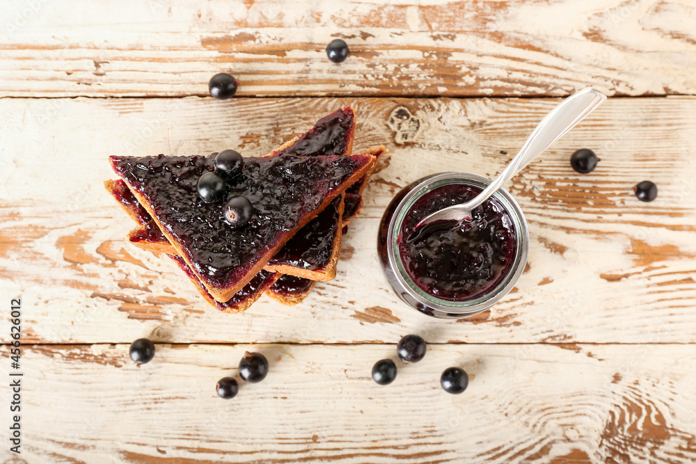 Jar and toasts with black currant jam on light wooden background