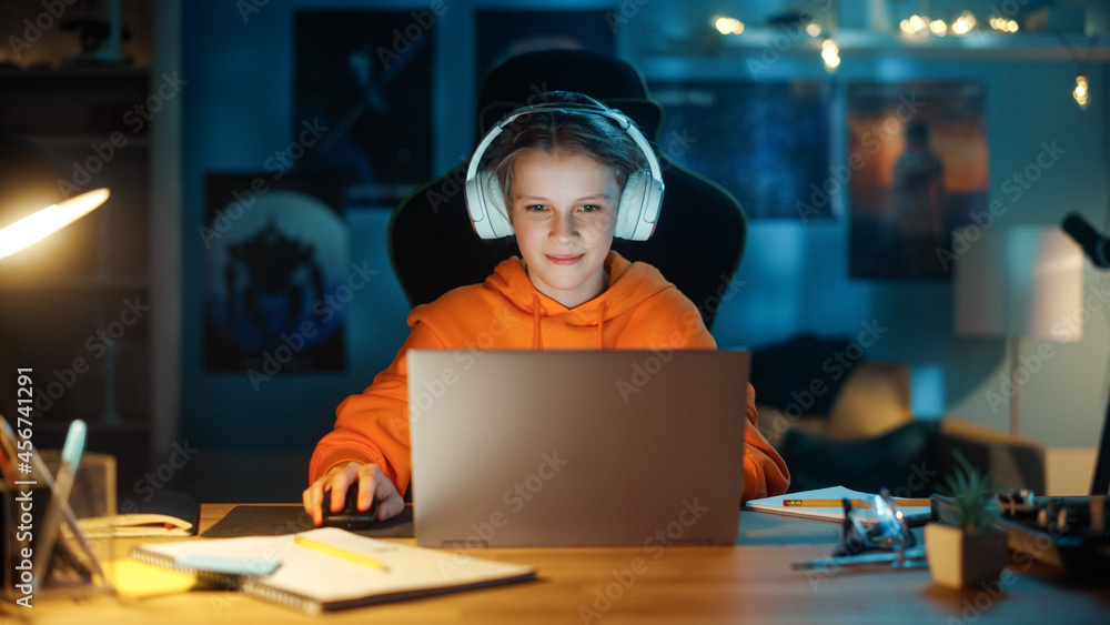 Smart Young Boy in Headphones Using Laptop Computer in Cozy Dark Room at Home. Happy Teenager Browsi