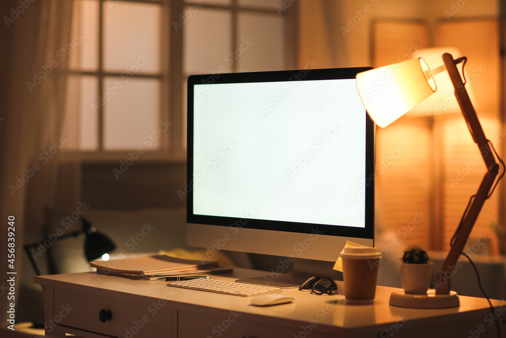 Modern computer, lamp and stationery on table in evening